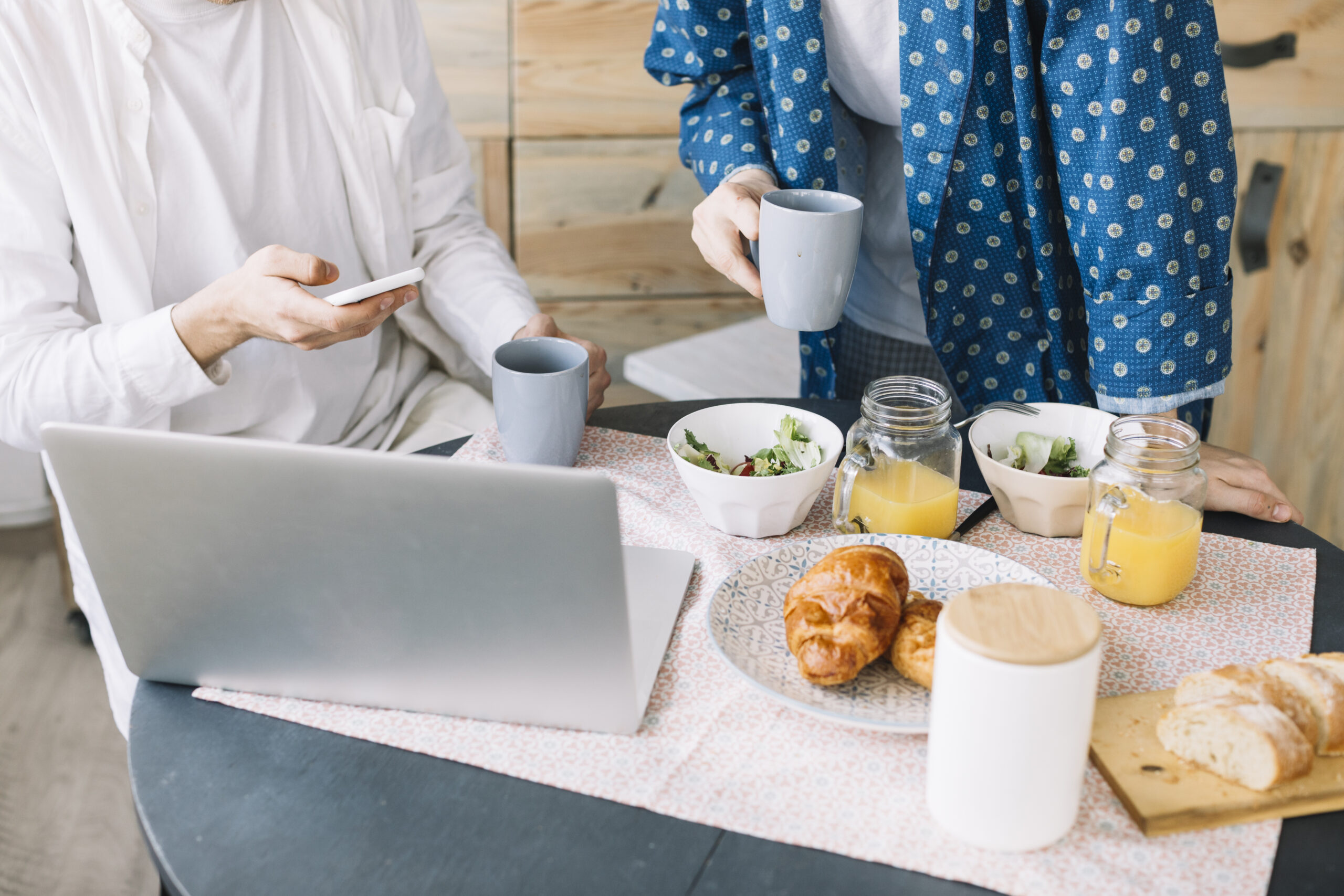 section mediane des hommes tenant une tasse de cafe pres de delicieux petit dejeuner avec jus et ordinateur portable sur une table en bois scaled
